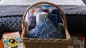 A bedroom with a bed, pillows, a fan, a basket of toiletries, and a magazine on a nightstand.