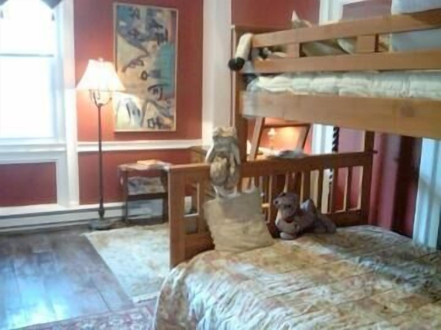 A room with a bunk bed, a small table, a lamp, and a painting on the wall.