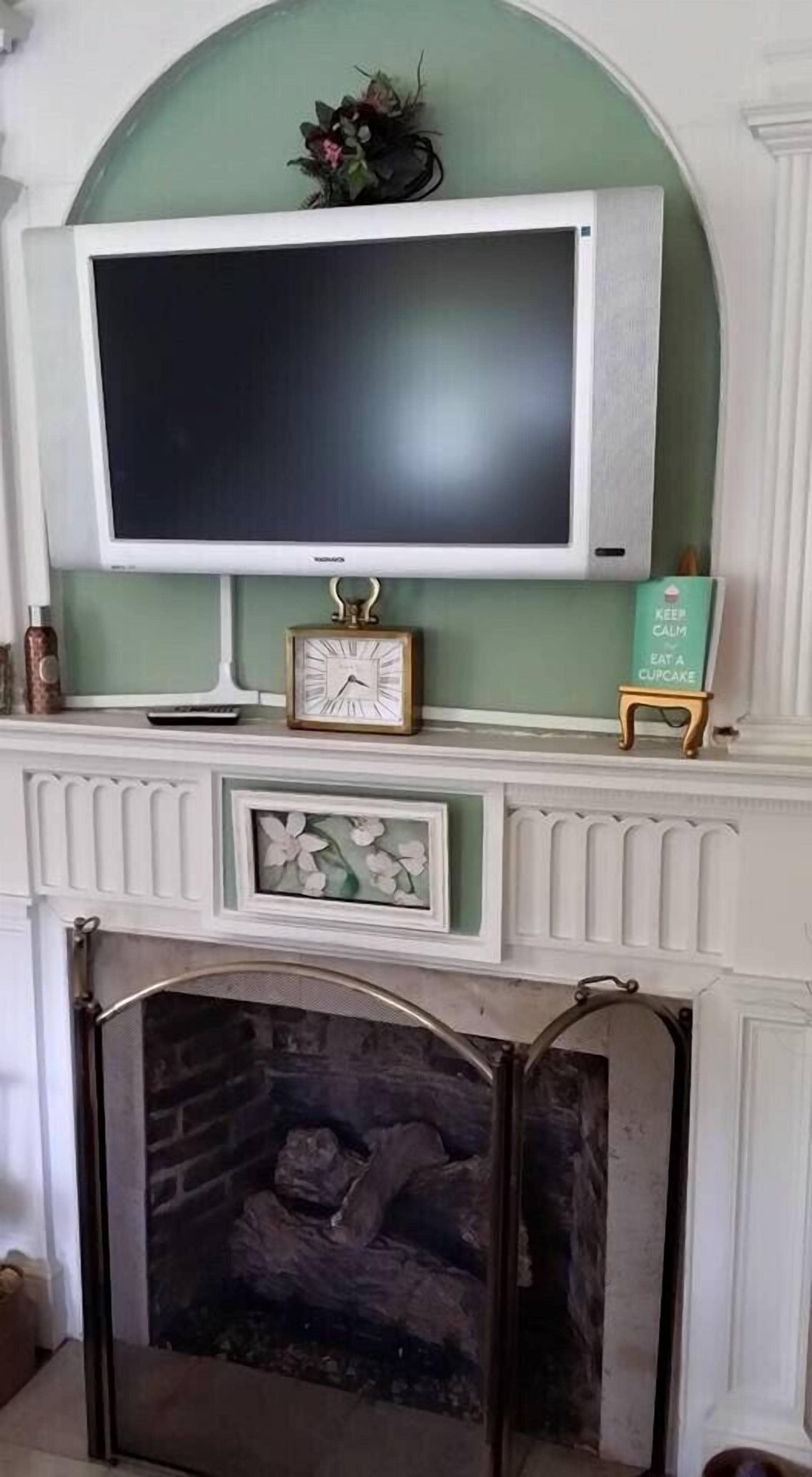 A fireplace with a modern TV mounted above it, a small clock, and a decorative sign.