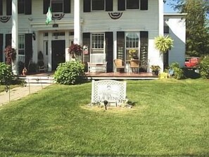 A two-story white building with a front porch, a flag, and a well-maintained lawn.