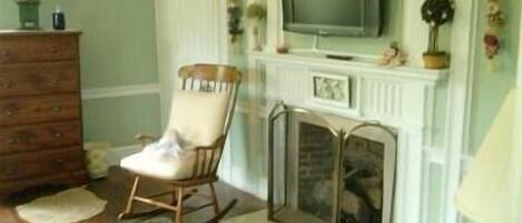 A room with a wooden dresser, a rocking chair, a fireplace, and a television mounted above it.