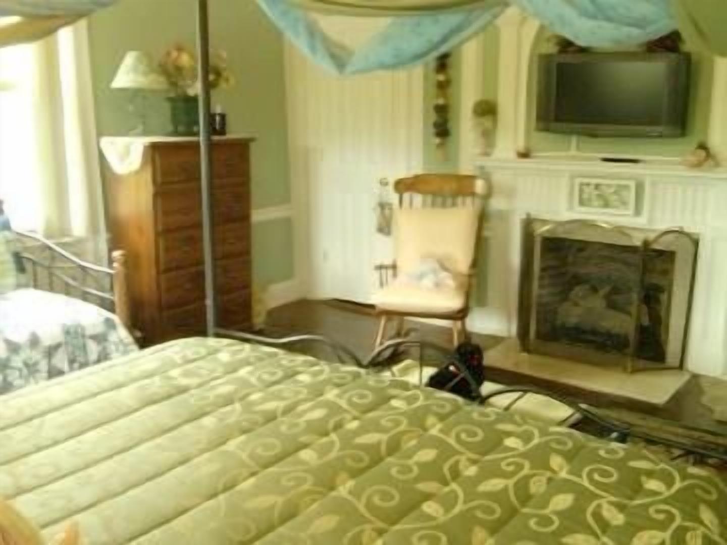 A bedroom with a bed, a chair, a television, and a fireplace.