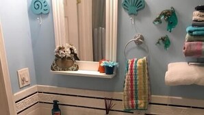 A bathroom with a white sink, mirror, and toilet. There are decorative items on the wall and a towel rack with towels.