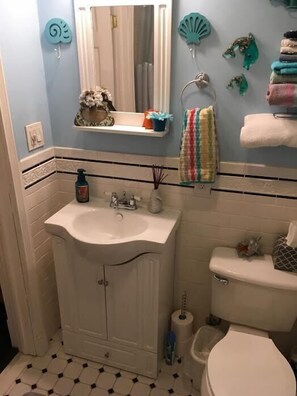 A bathroom with a white sink, mirror, and toilet. There are decorative items on the wall and a towel rack with towels.