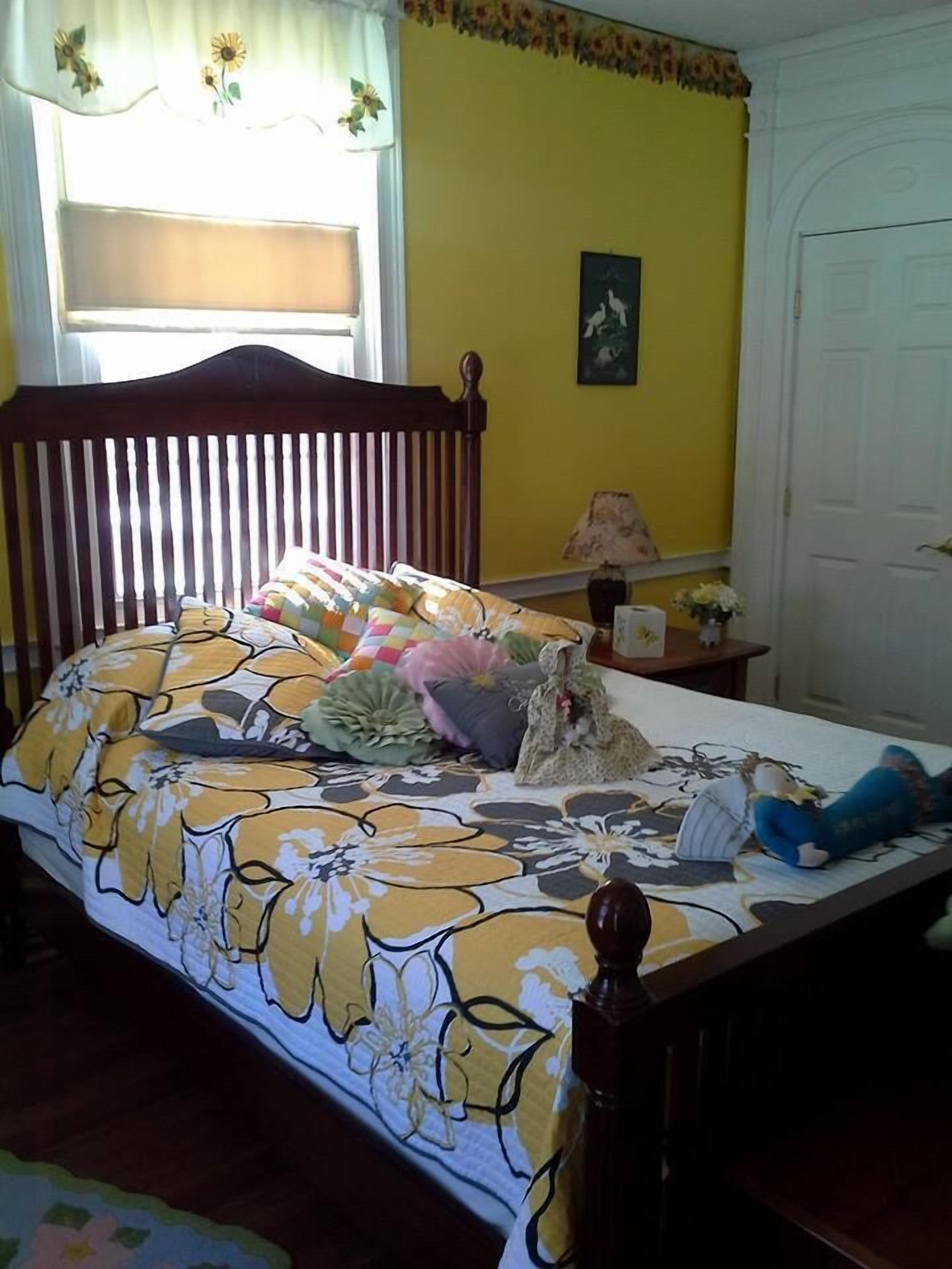 Une chambre à coucher avec un lit en bois, une literie à motifs floraux, une table de chevet avec une lampe et un tableau accroché au mur.