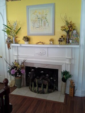 A fireplace with a mantel decorated with various items, including a framed picture, small figurines, and potted plants. - Brookside Inn At Laurens (Laurens)