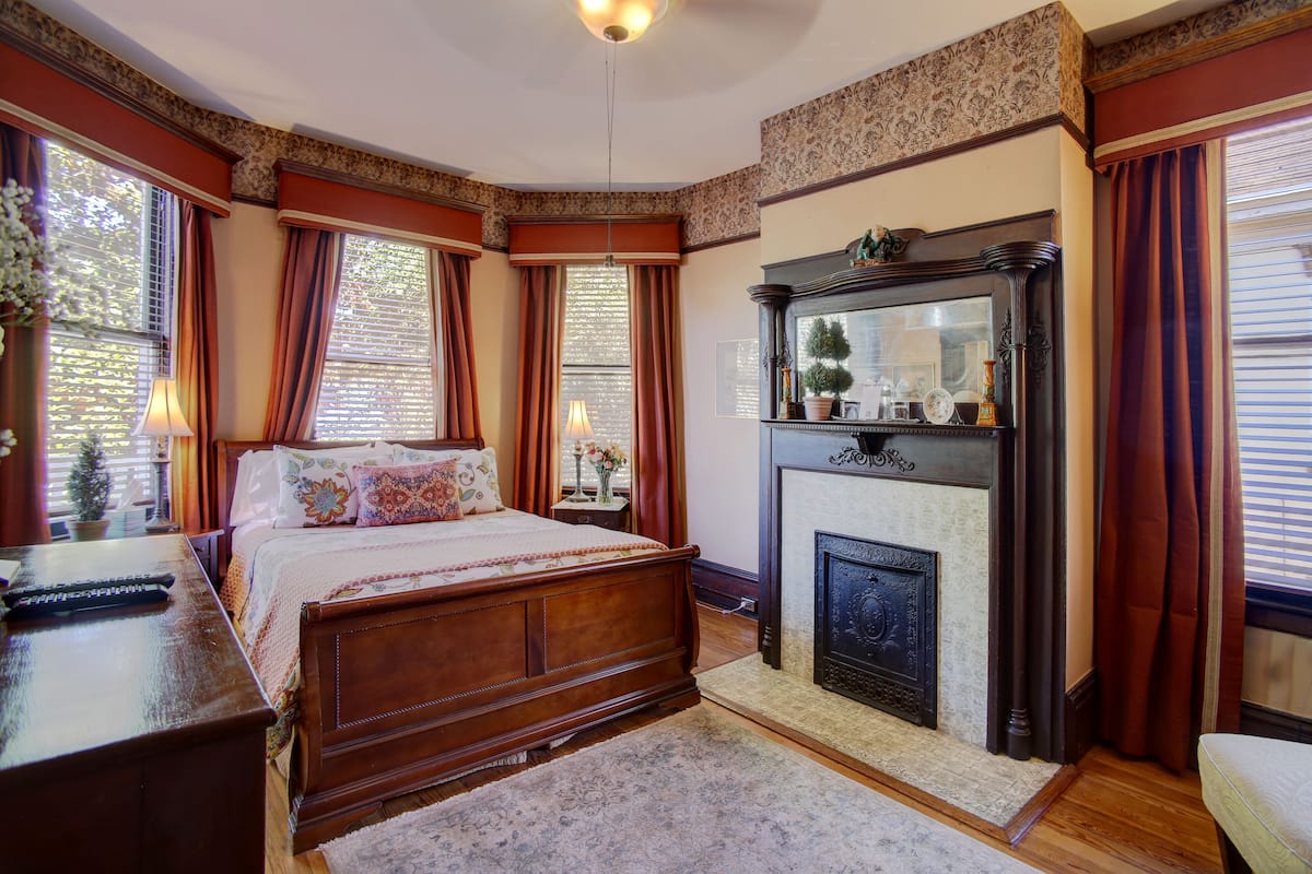 A bedroom with a large bed, a fireplace, and a nightstand with a lamp.