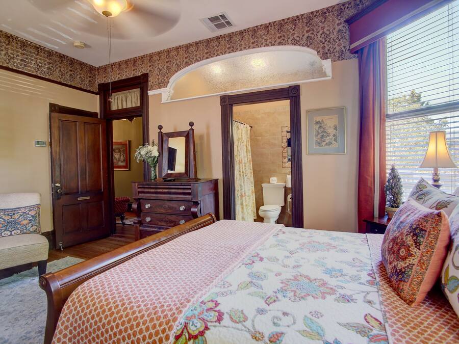 Quarto com cama, penteadeira e banheiro visível por um arco.
