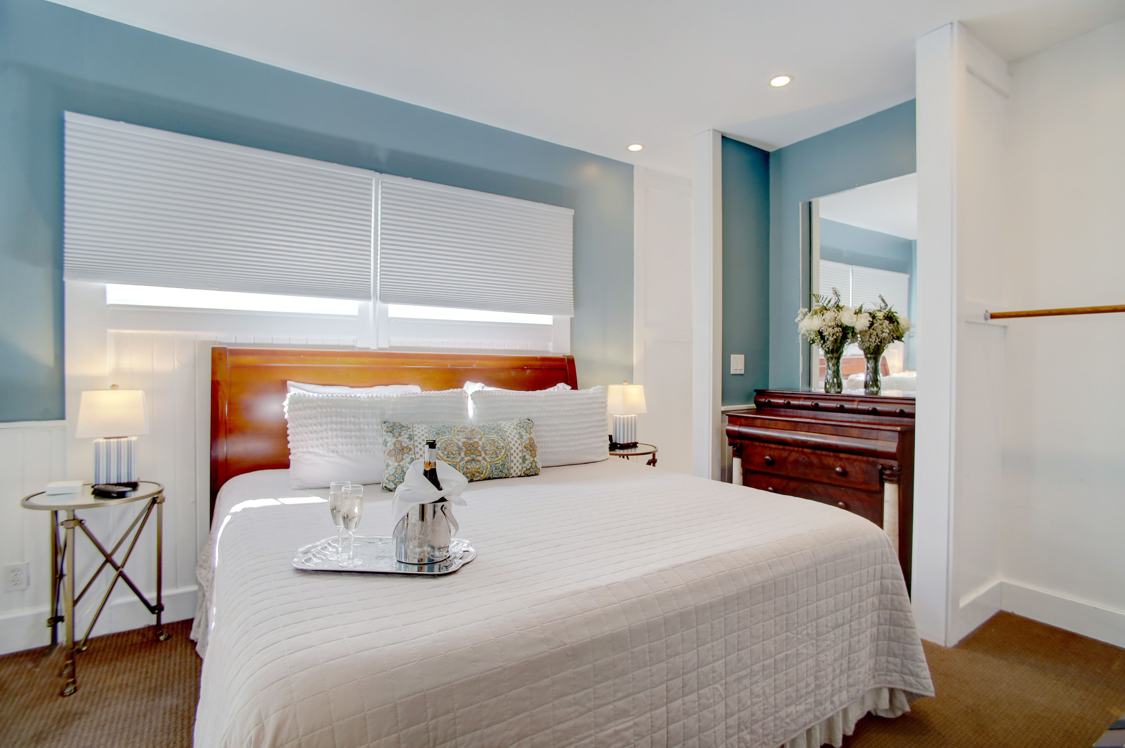 A hotel room with a large bed, bedside lamps, a wooden dresser, and a mirror.