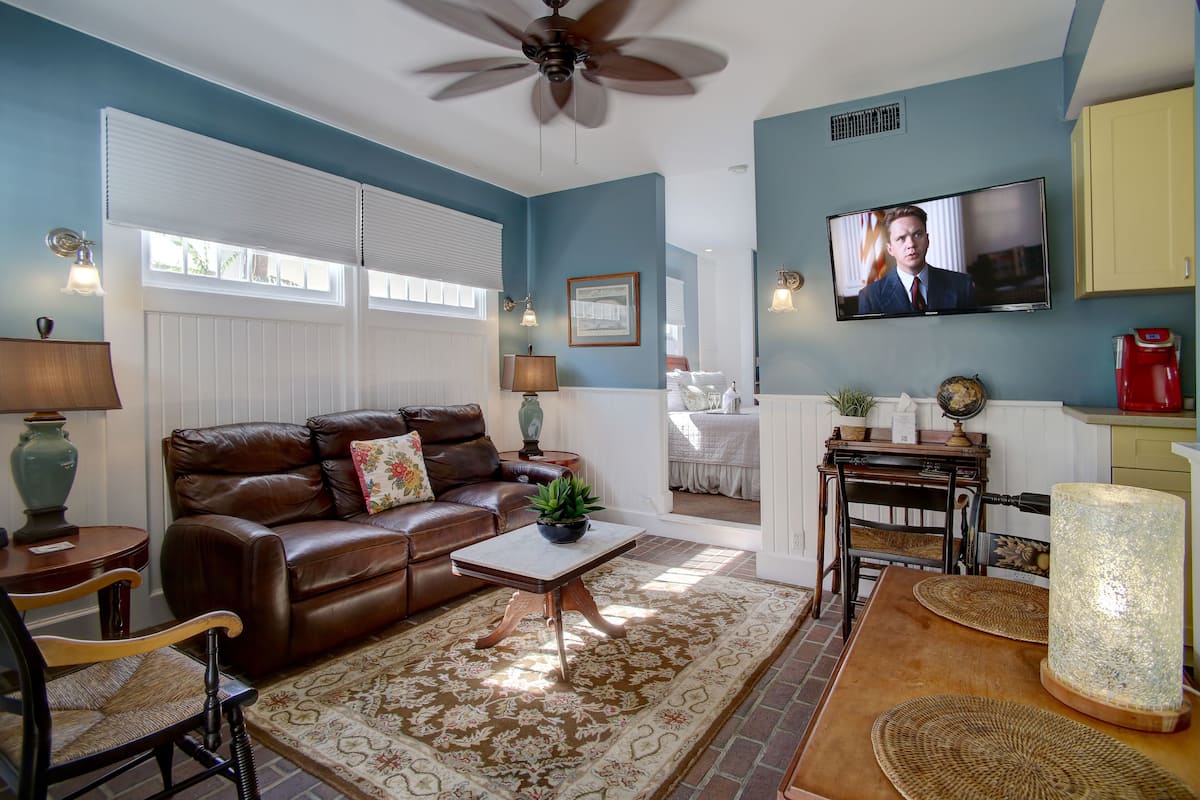 A living room with a brown leather sofa, a coffee table, a television, and a dining area with a table and chairs.