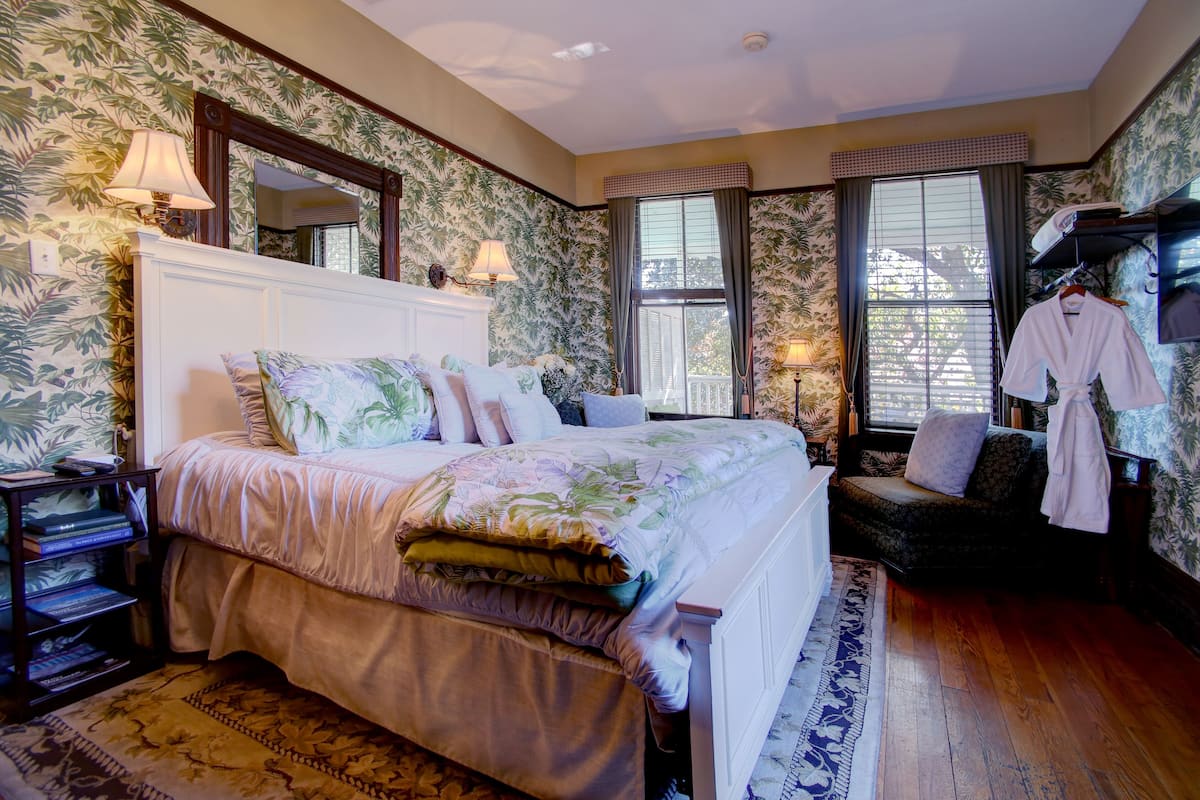 A bedroom with a large bed, a nightstand, a dresser, a chair, and a window with a view.