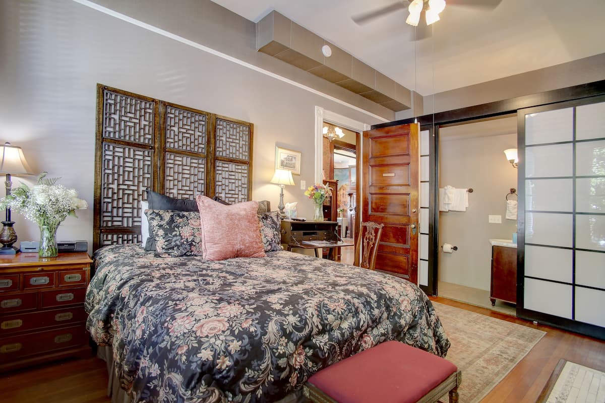 A bedroom with a large bed, wooden headboard, a dresser, and a sliding door leading to a bathroom.