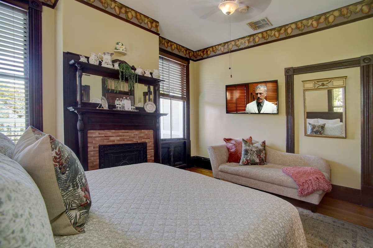 A bedroom with a large bed, a fireplace, a television, and a sofa.