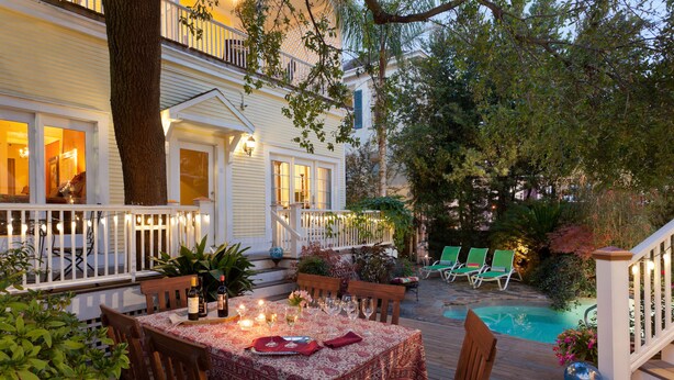 A wooden deck with a dining table set for six, surrounded by chairs and a pool.