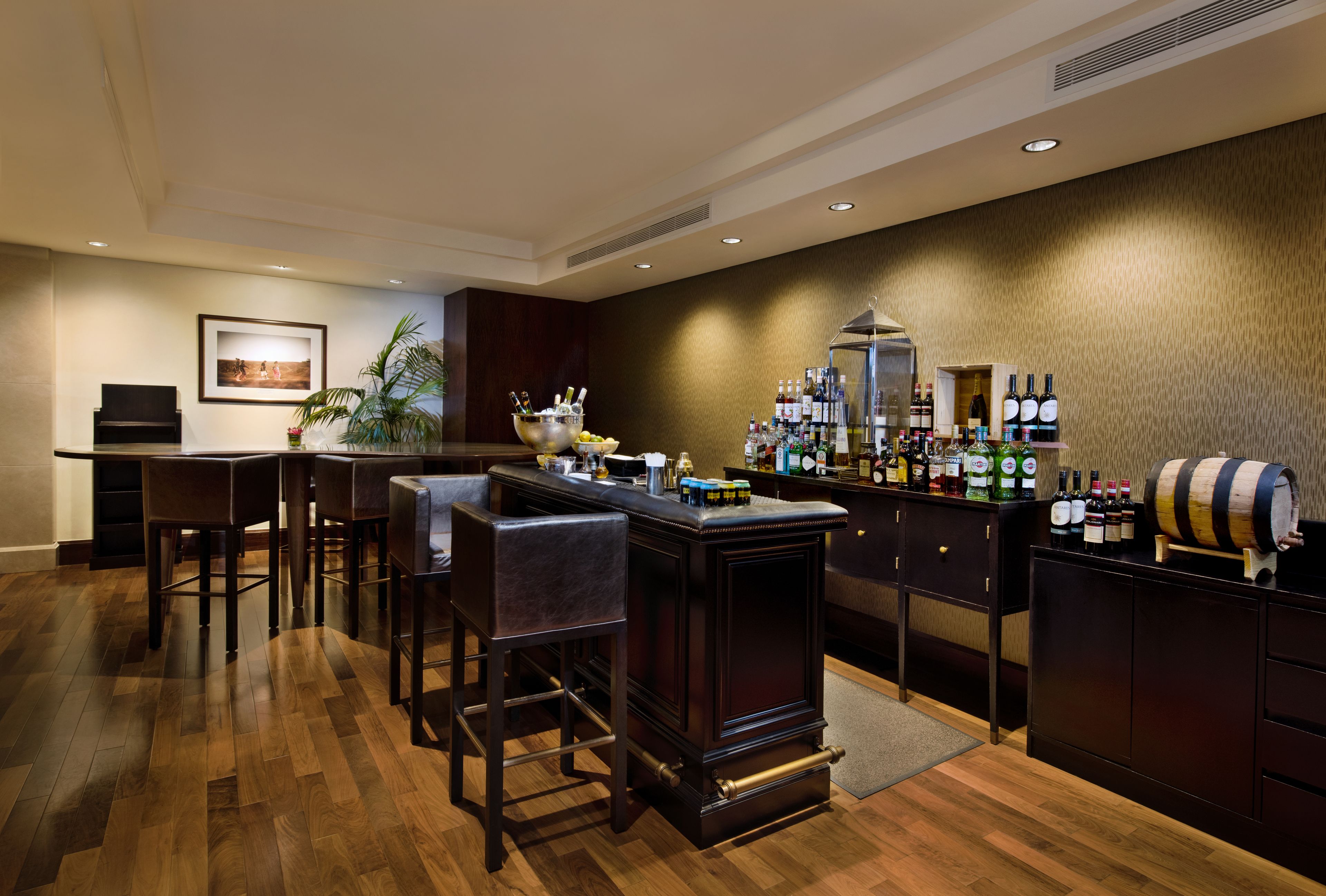 Zona de bar con suelo de madera, taburetes, un piano y una variedad de botellas y un enfriador de vino.