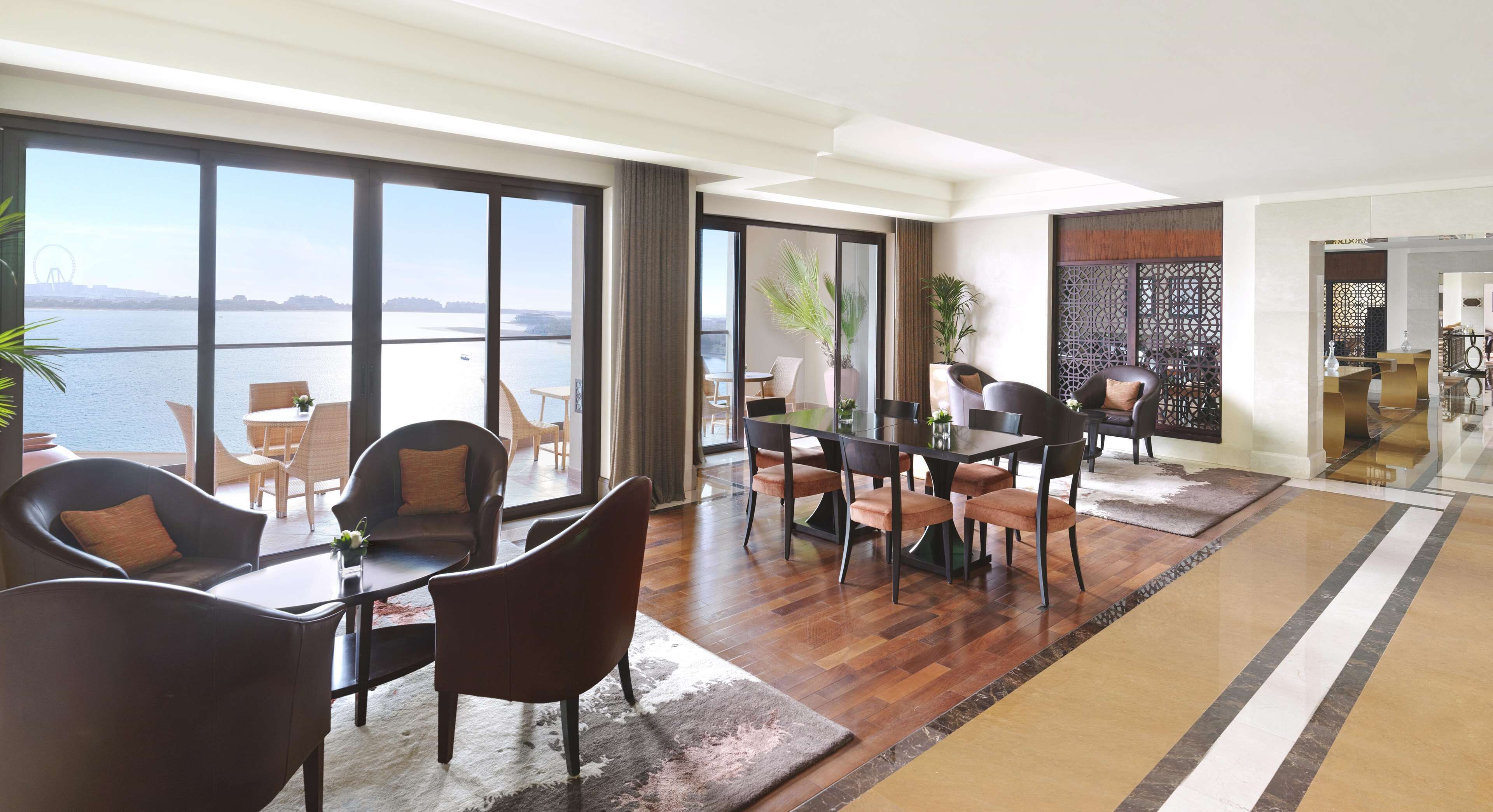 A spacious living area with a large window overlooking a body of water, furnished with modern chairs and a dining table.