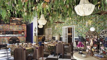 A room with a checkered floor, wicker furniture, hanging plants, and a decorative chandelier.