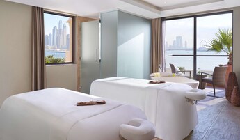 A hotel room with two beds, a balcony with a view of the city skyline, and a table with amenities.