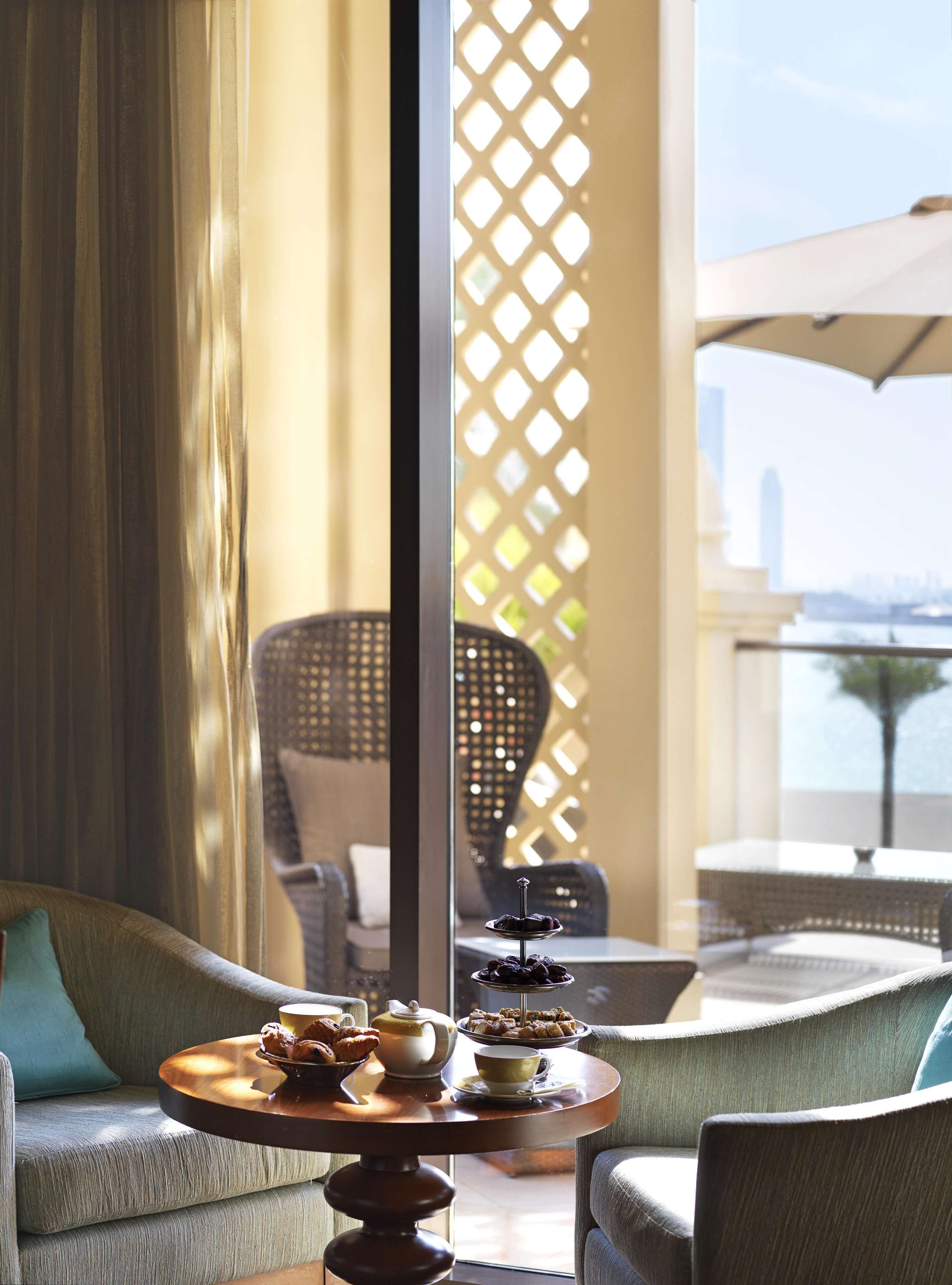 A cozy seating area with a round table set for tea, a wicker chair, and a view of the city skyline through a window.