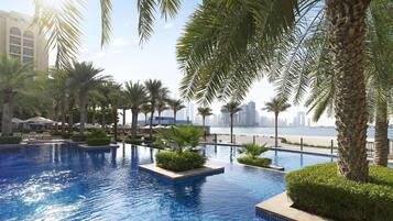 A pool area with palm trees, a view of the city skyline, and a body of water.