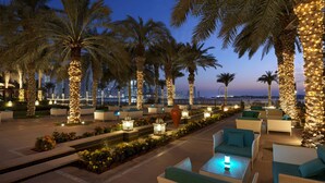 A well-lit outdoor seating area with palm trees and a view of the city skyline at dusk.