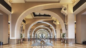 A spacious, well-lit lobby with high ceilings and arches, featuring a central decorative table and potted plants.