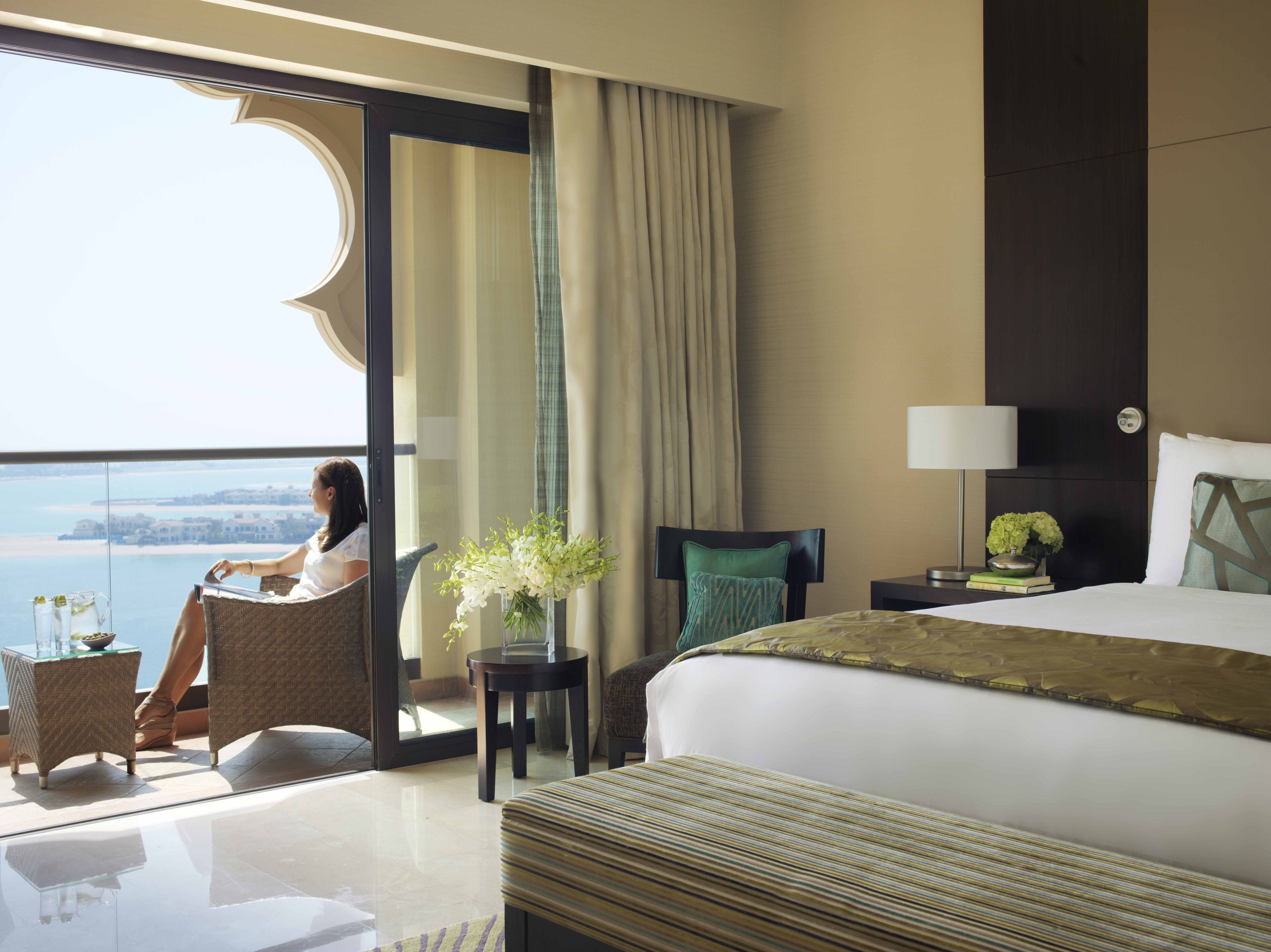 Hotelkamer met een groot bed, uitzicht op zee, een balkon en een zithoek met een tafel en stoelen.