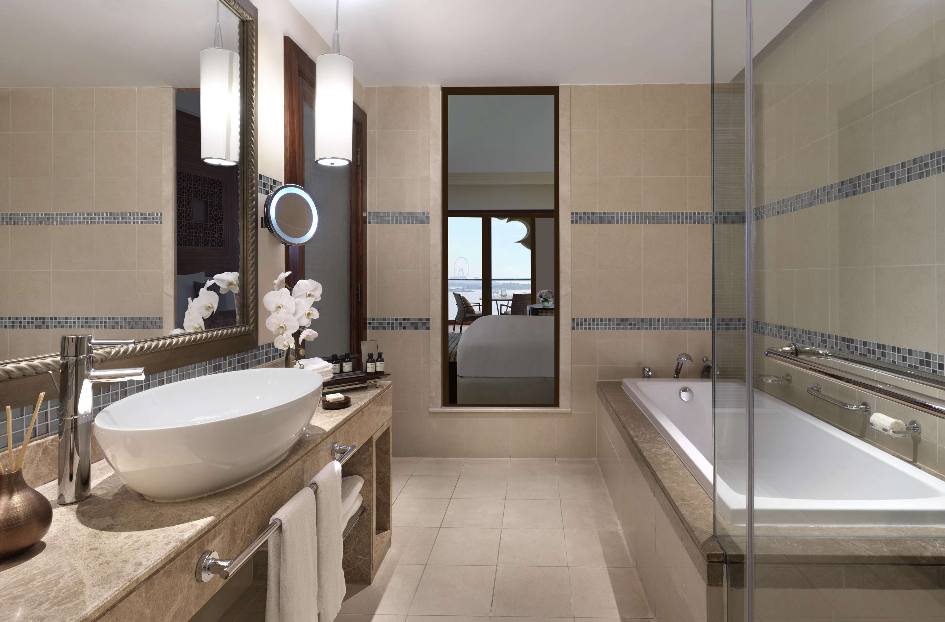 Un baño moderno con un lavamanos ovalado grande, una ducha con cerramiento de vidrio y un espejo grande con un espejo redondo encima.