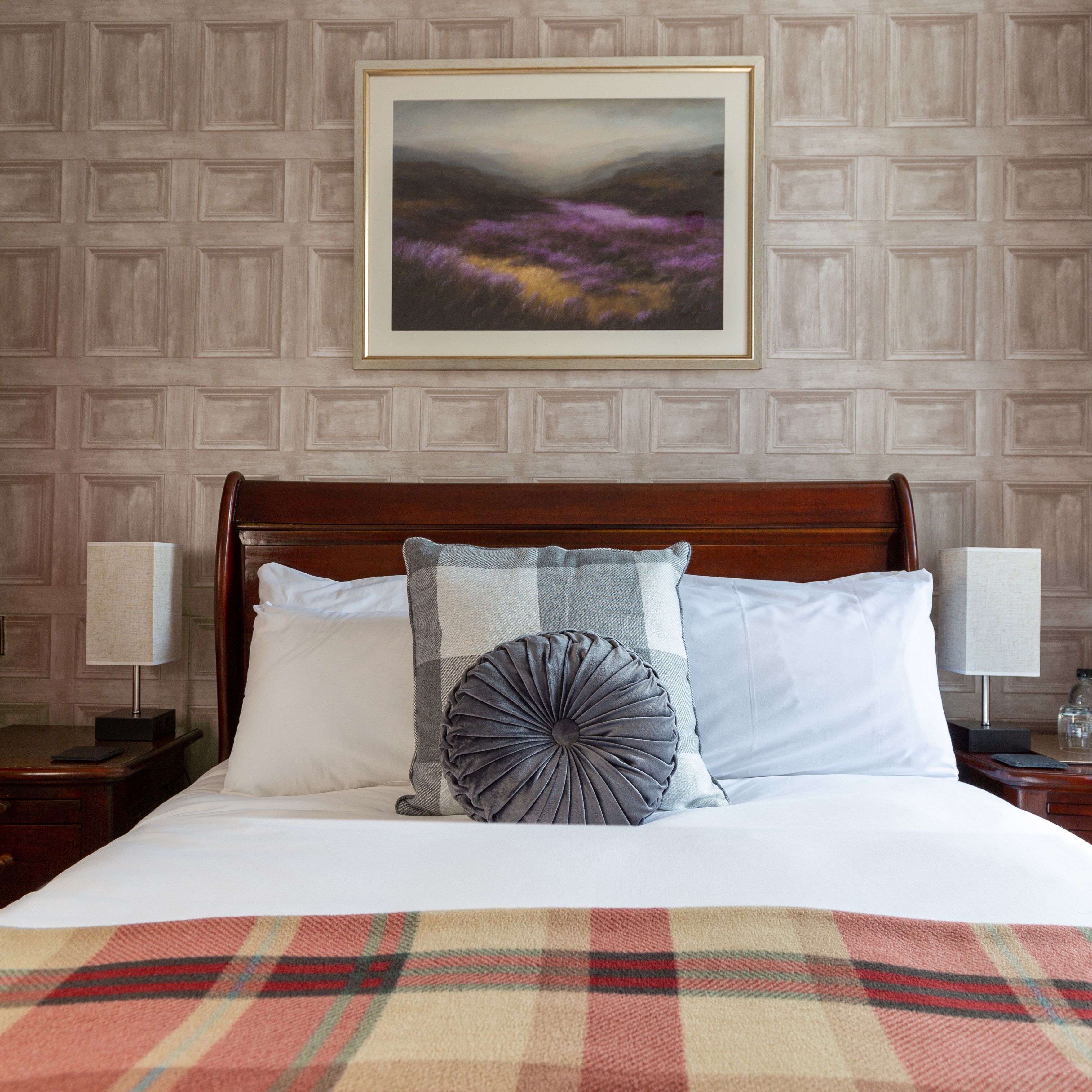 Cama arrumada com coberta xadrez, travesseiro quadriculado e travesseiro decorativo. Um quadro emoldurado pendurado acima da cama.