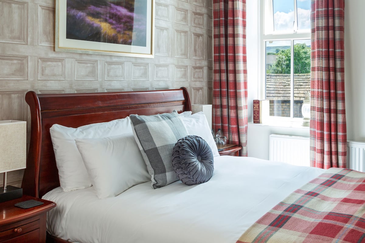 A neatly made bed with white and grey bedding, a wooden headboard, and a plaid throw blanket.