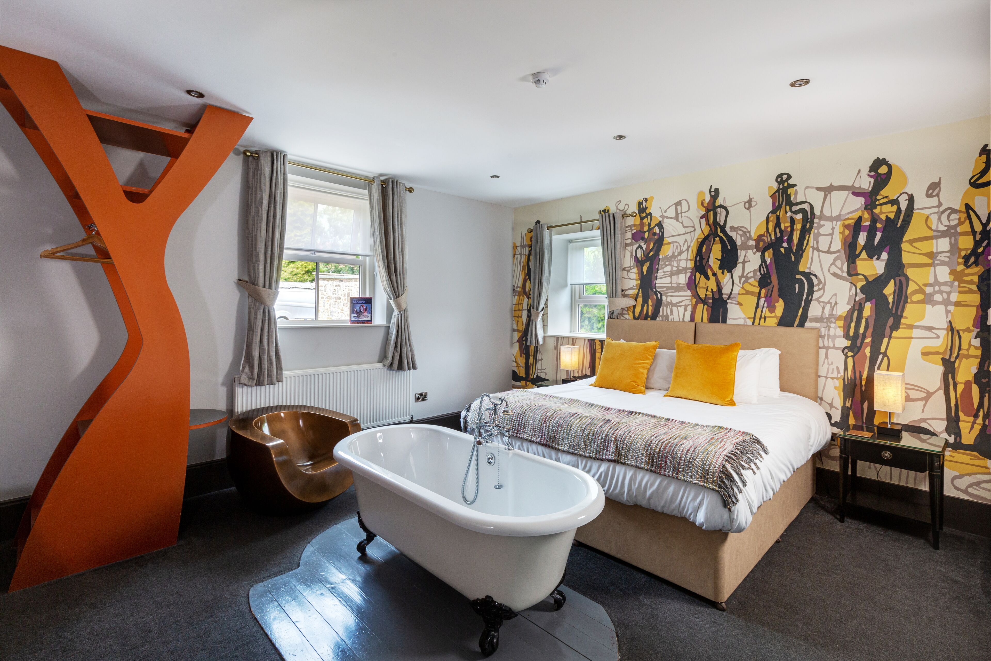 Une chambre à coucher moderne avec un grand lit, une baignoire sur pieds et une fresque murale originale.
