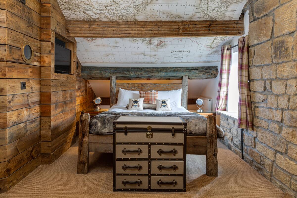 A rustic wooden room with a bed, a map on the ceiling, and a stone wall.