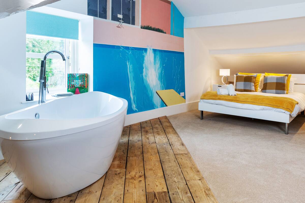 A modern bathroom with a freestanding bathtub, a wooden floor, and a large window.