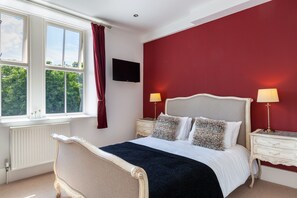 A bedroom with a large bed, two bedside tables with lamps, a TV on the wall, and a window with curtains. - The Craven Heifer Addingham (Ilkley)