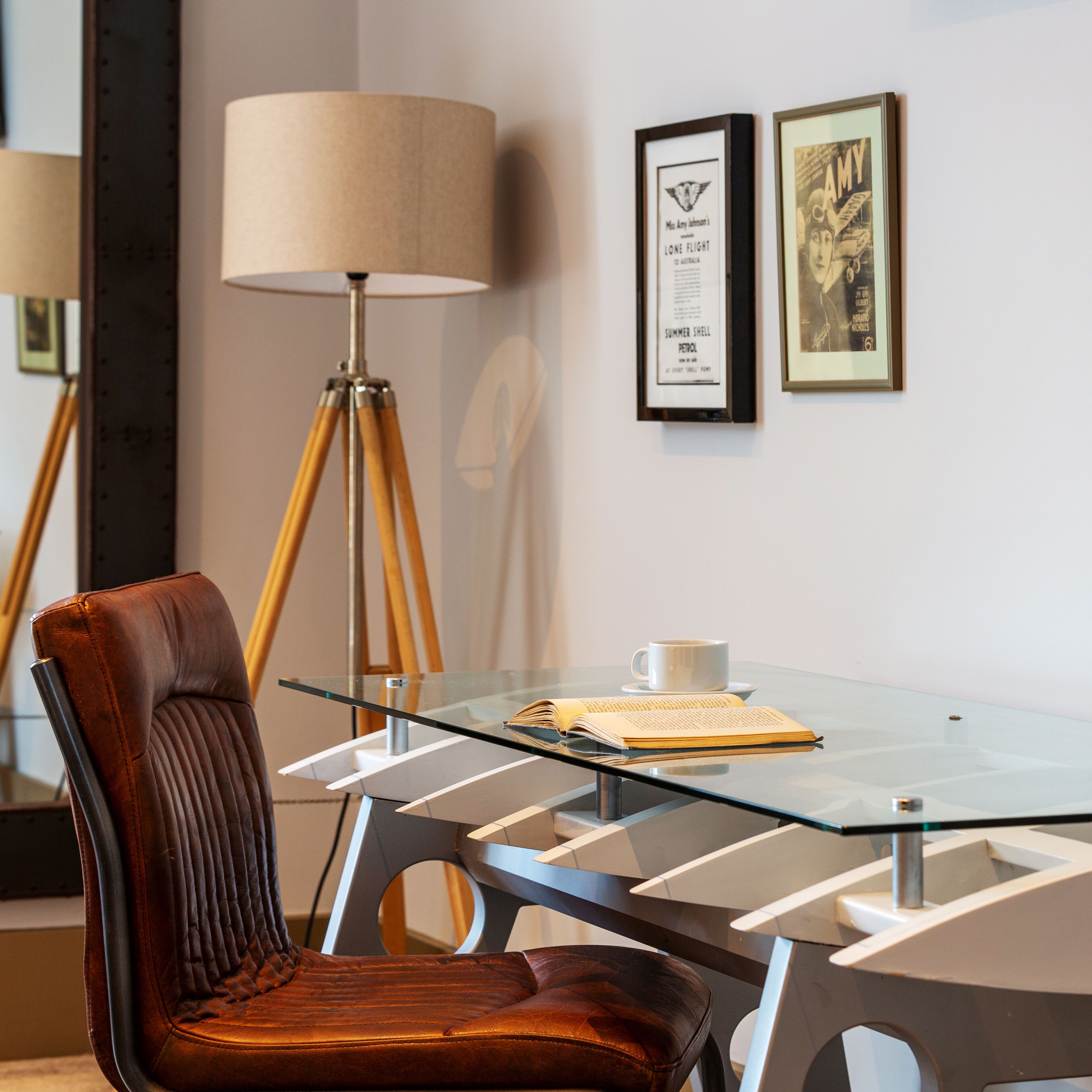 Una sala de conferencias moderna con una mesa de vidrio, un sillón de cuero y una lámpara de pie.