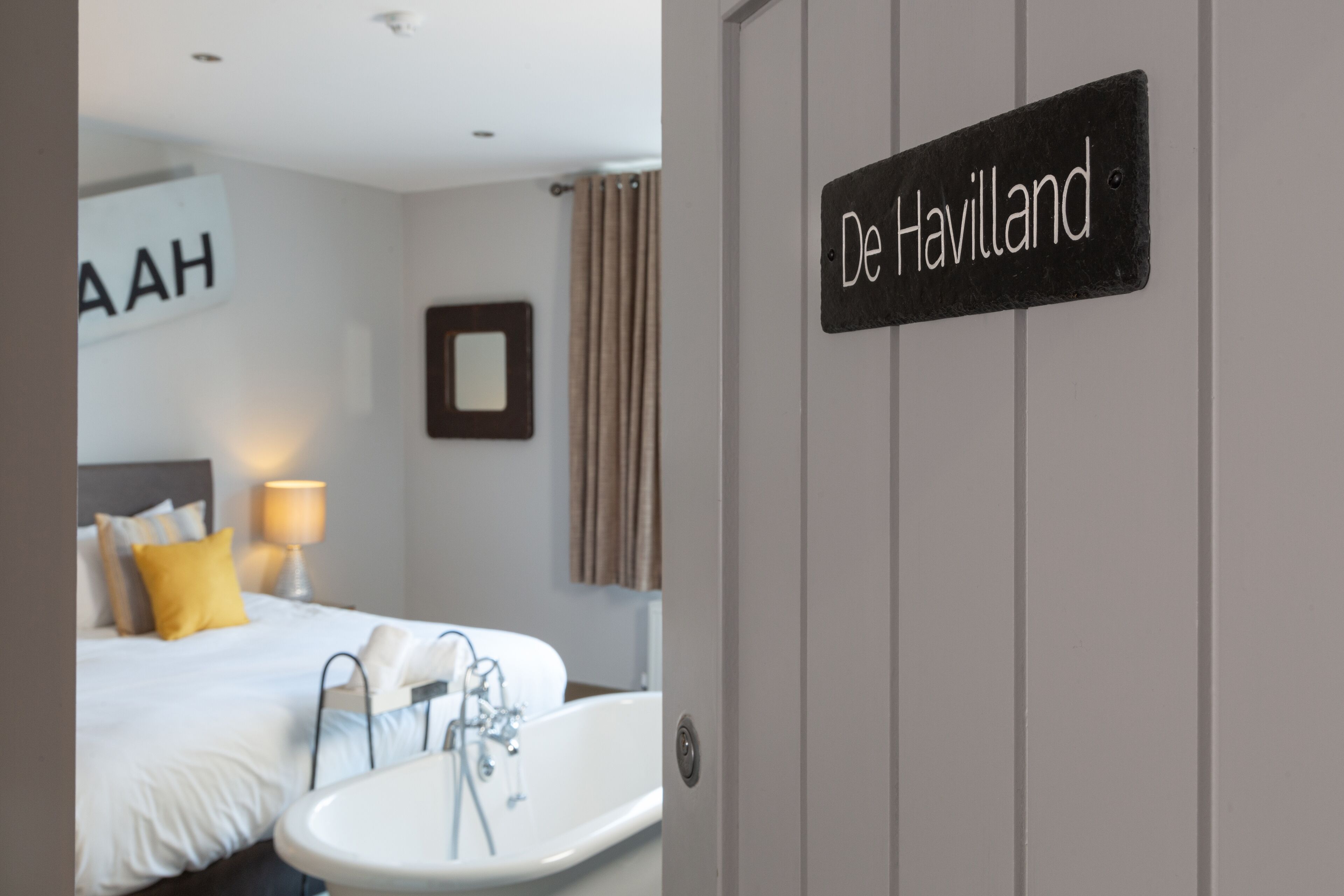 A hotel room with a bed, a white bathtub, and a sign reading "De Havilland".