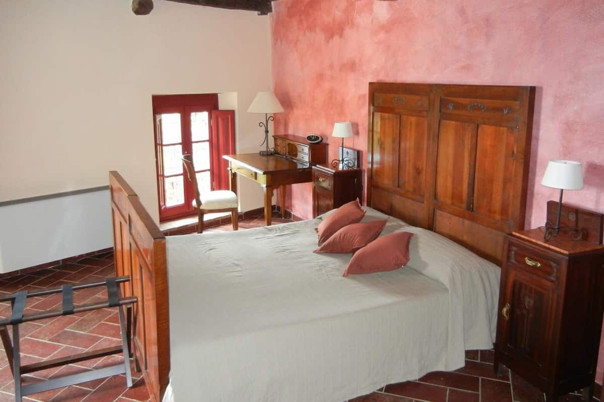 A bedroom with a bed, a desk, a chair, a wardrobe, and a window with red curtains.
