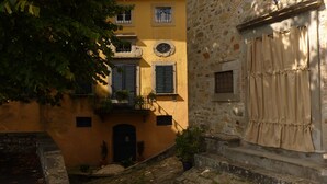 A building with a yellow facade, stone walls, and a balcony with potted plants. - San Gennaro Castello (Capannori)