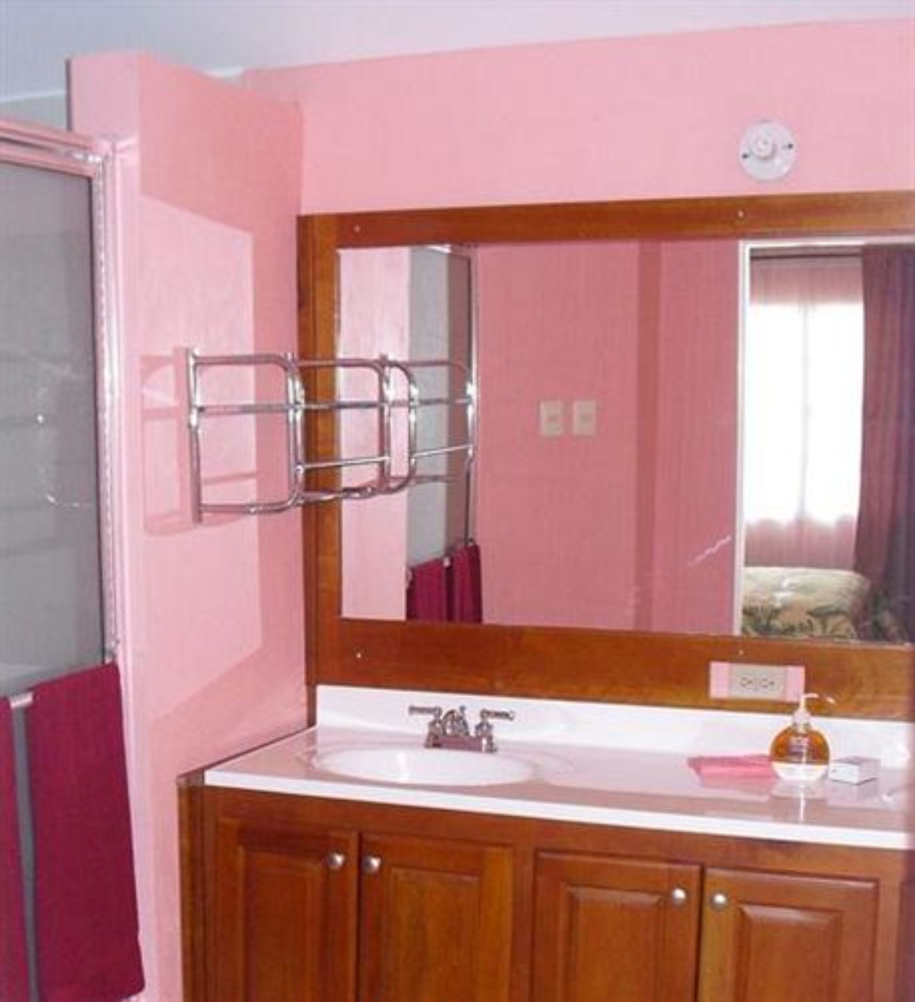 A bathroom with a pink wall, wooden cabinets, a white sink, and a mirror with a towel rack.