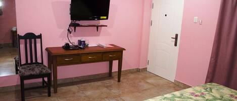 A bedroom with a bed, a desk with a chair, a television, and a door.