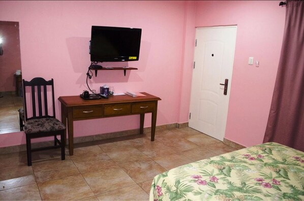 A bedroom with a bed, a desk with a chair, a television, and a door.