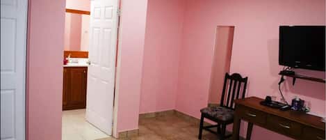 A room with pink walls, a wooden desk with a chair, a television, and an air conditioning unit.