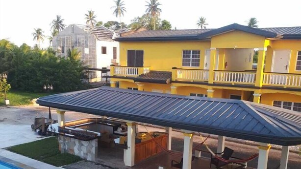 A yellow building with a covered outdoor seating area and a swimming pool. - Piarco Village Suites (Piarco)