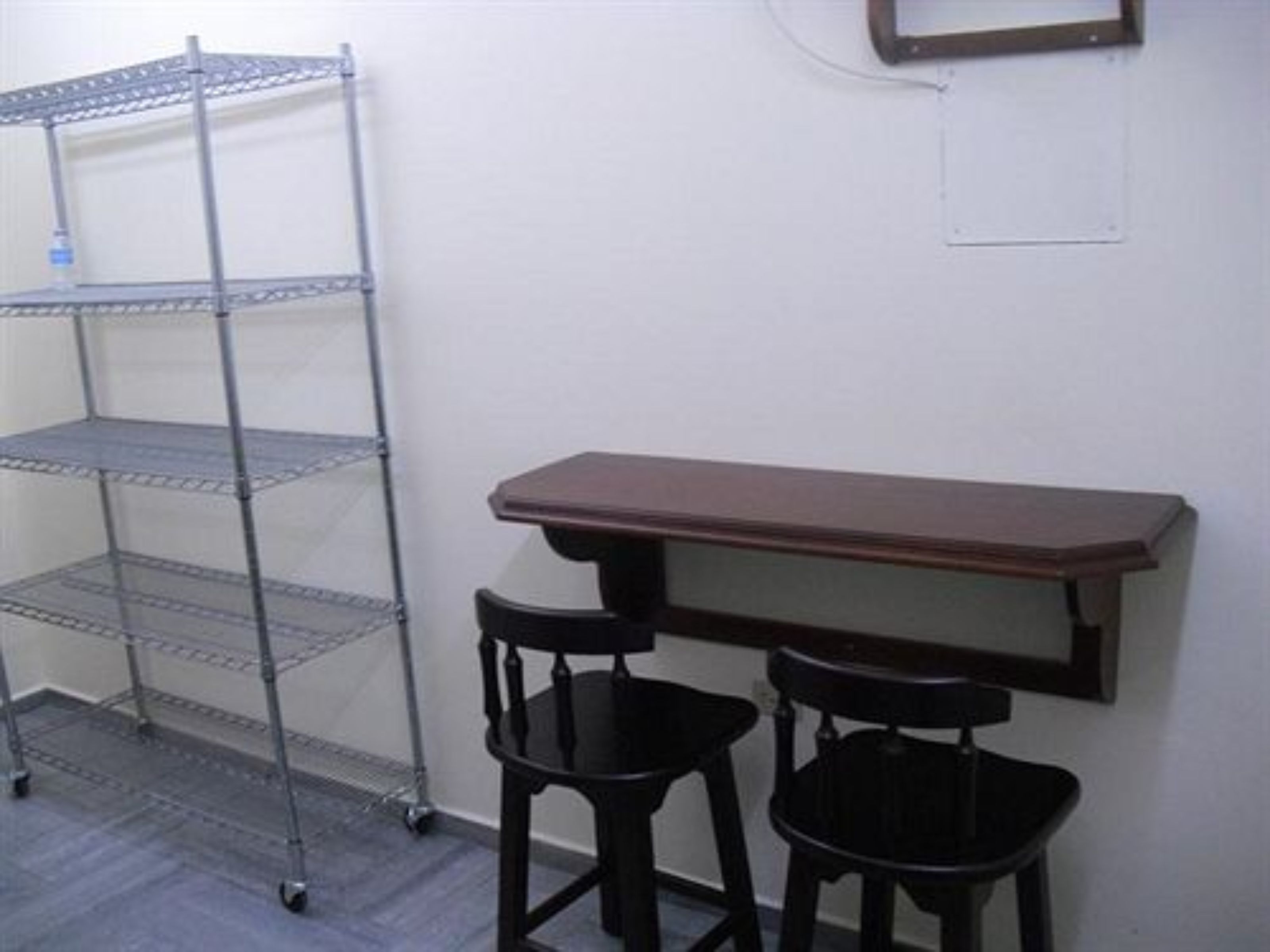 A room with a metal shelving unit, a wooden table, and two black chairs.