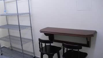 Una habitación con una estantería metálica, una mesa de madera y dos sillas negras.