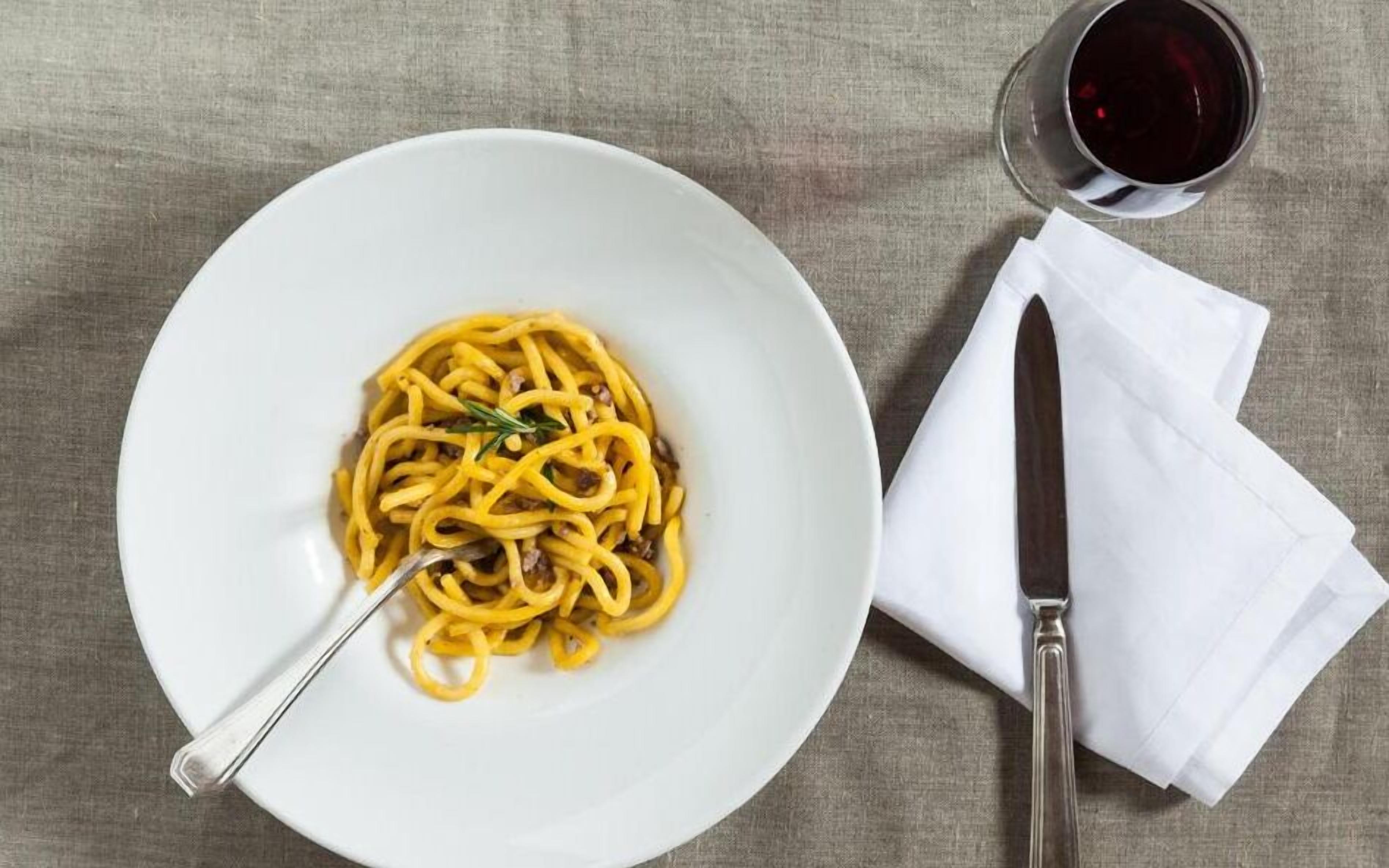 Un piatto di spaghetti con una forchetta, un tovagliolo e un bicchiere di vino rosso su una superficie strutturata.