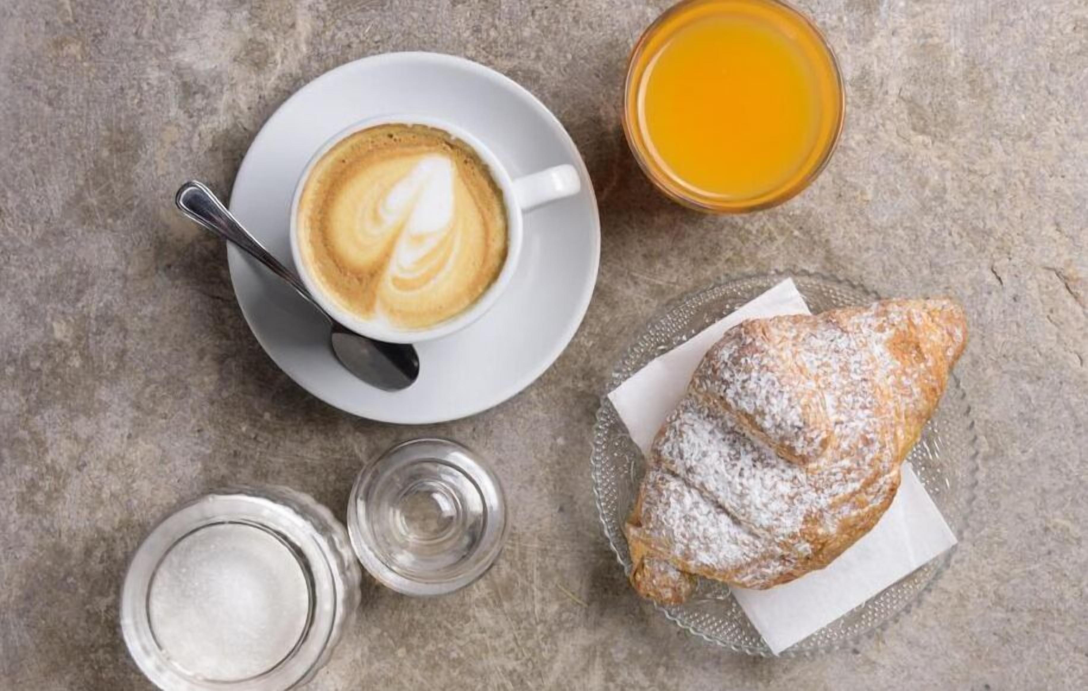 Una mesa con una taza de café, un vaso de jugo de naranja, un pastel y dos vasos de agua.