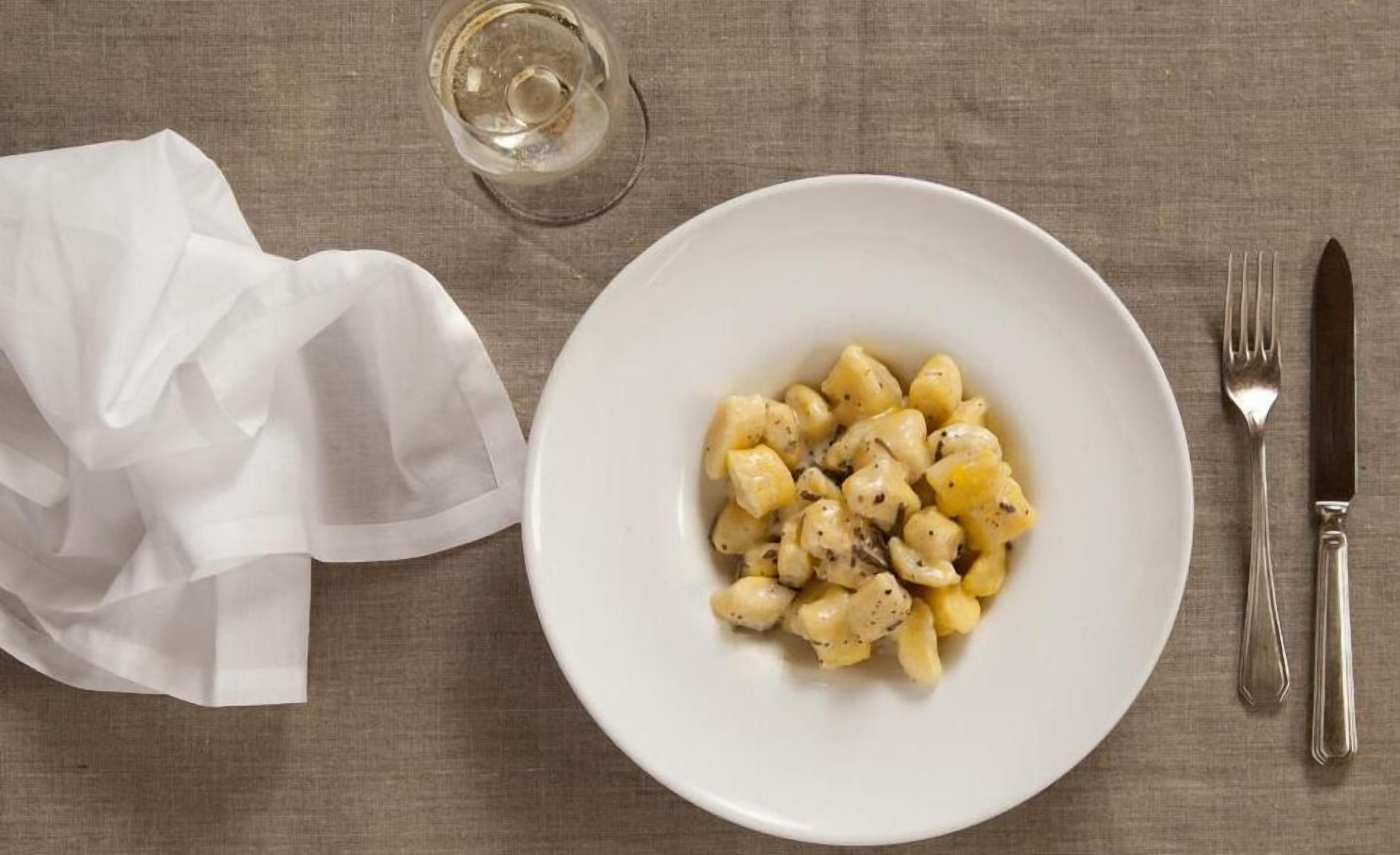 Un plato de ñoquis con un tenedor y cuchillo a un lado, sobre una mesa.