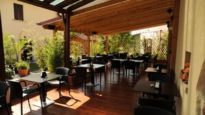 An outdoor patio with wooden tables and chairs, surrounded by greenery and a wooden pergola. - Albergo Scaldaferro (Sandrigo)