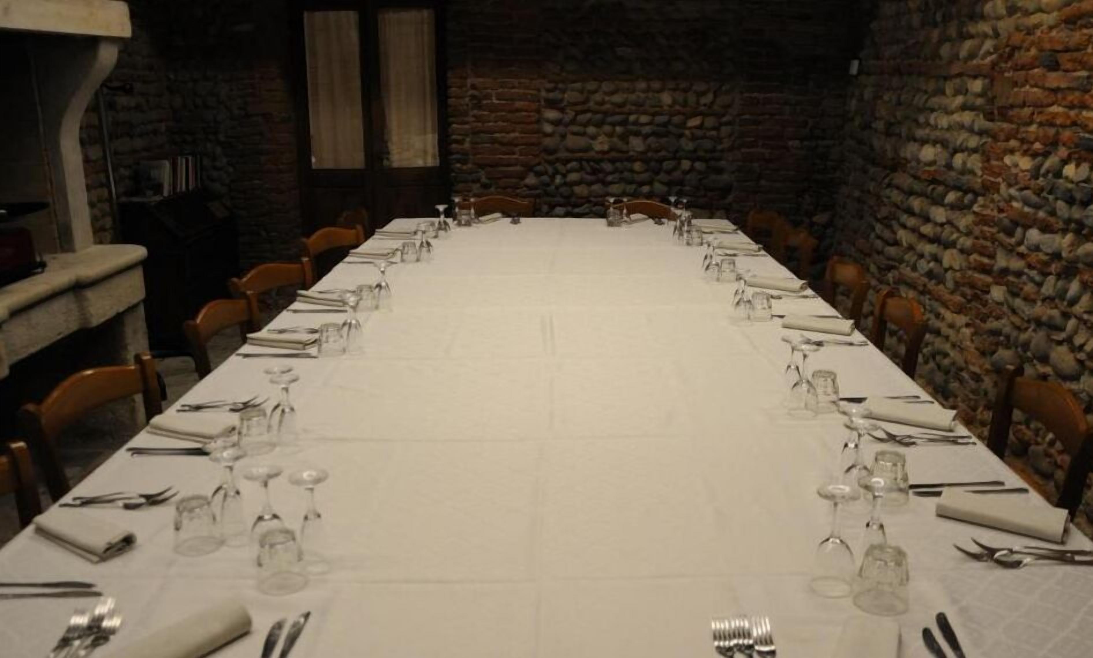 Una larga mesa de comedor cubierta con manteles blancos, cristalería y cubiertos, rodeada de paredes de piedra.